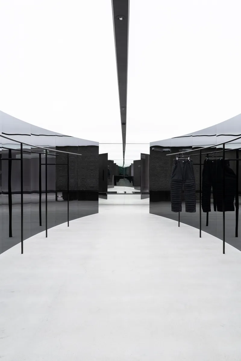 Central aisle framed by black metal garment racks beneath linear skylight slot in white ceiling