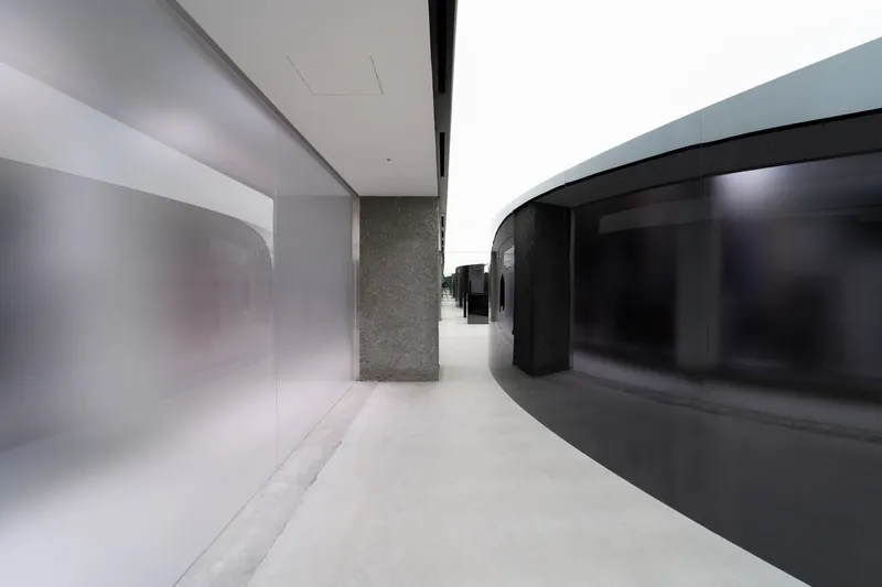 Curved circulation corridor with black glass facade, terrazzo column, and polished white resin floor