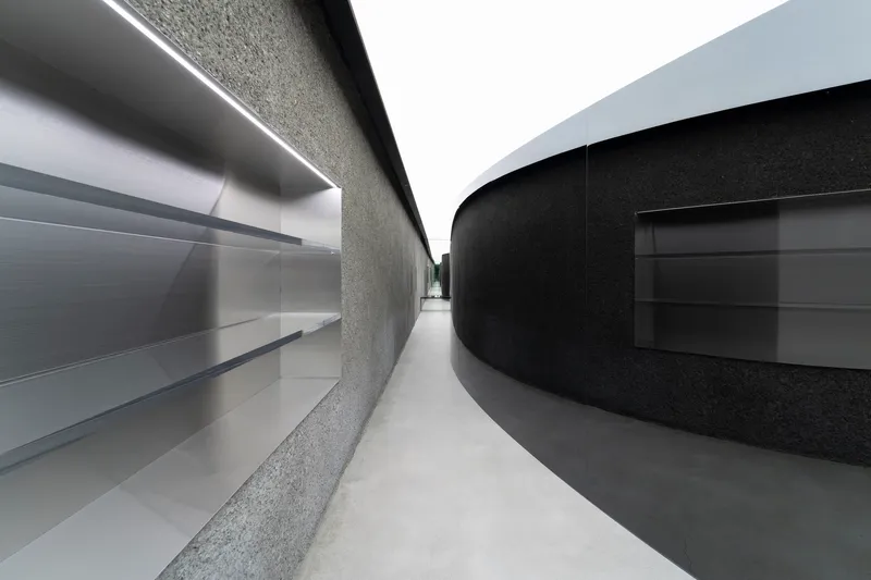 Narrow passage between curved terrazzo wall and black metal display with linear ceiling lighting