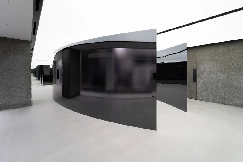 Interior gallery with curved black glass partition and textured grey stone walls under white ceiling planes