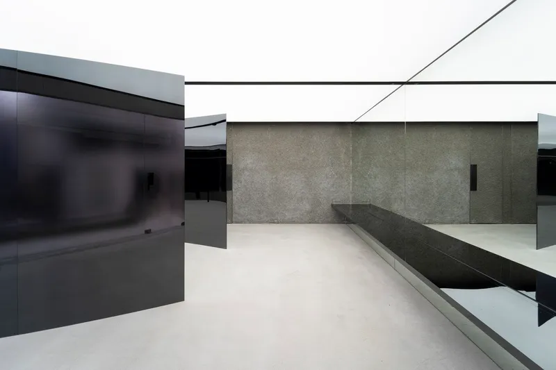 Angular black glass partitions intersecting with textured stone wall and built-in seating bench on polished floor