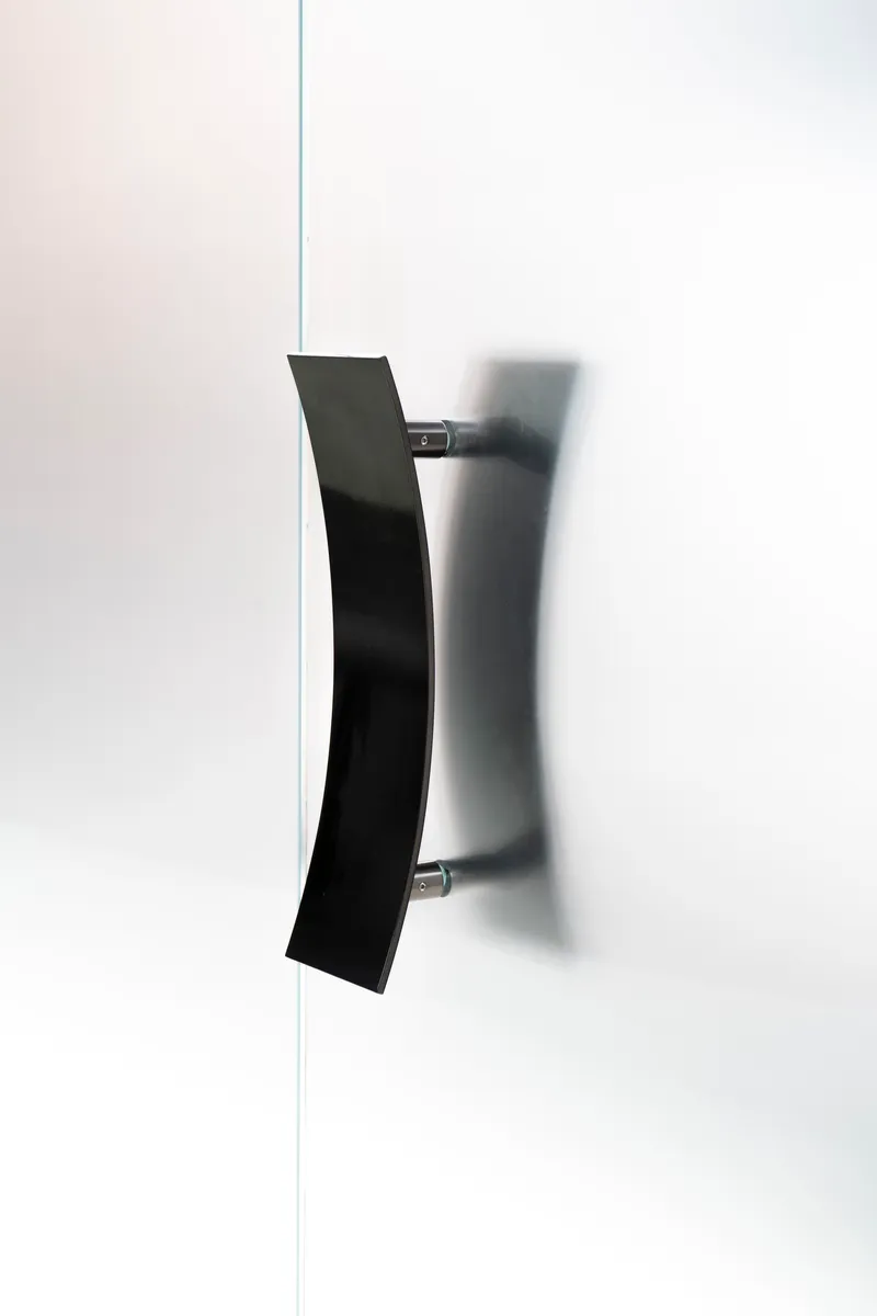 Angled black metal door handle mounted on white wall casting diagonal shadow