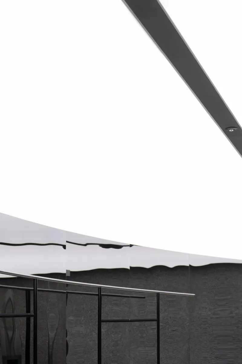 View of undulating white ceiling edge meeting textured dark stone wall with steel-framed glazing below