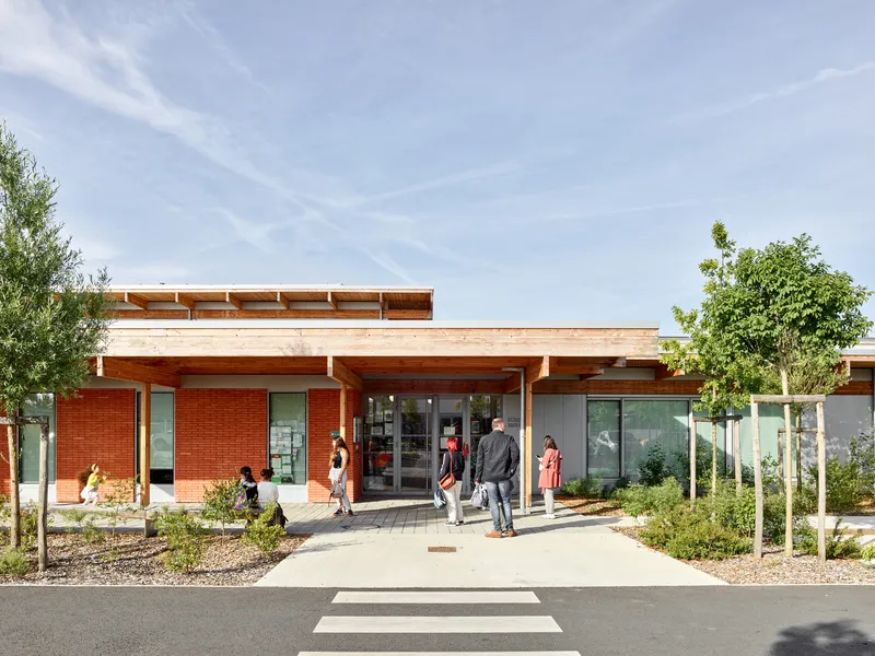 Main entrance with timber canopy over glass doors and red brick facade under overcast sky