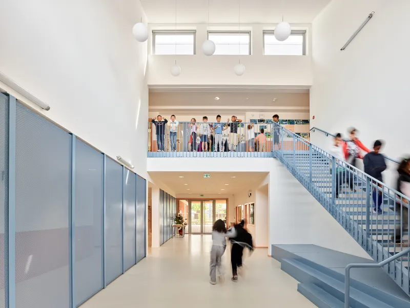 Double-height circulation hall with blue perforated metal staircase and children moving through the space