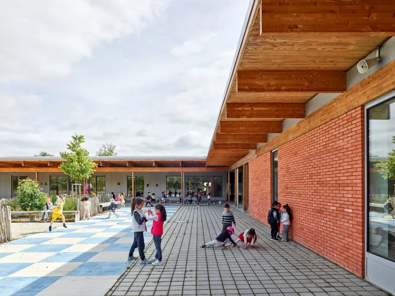 Outdoor courtyard with red brick wall and dark decking where children play under a cloudy sky
