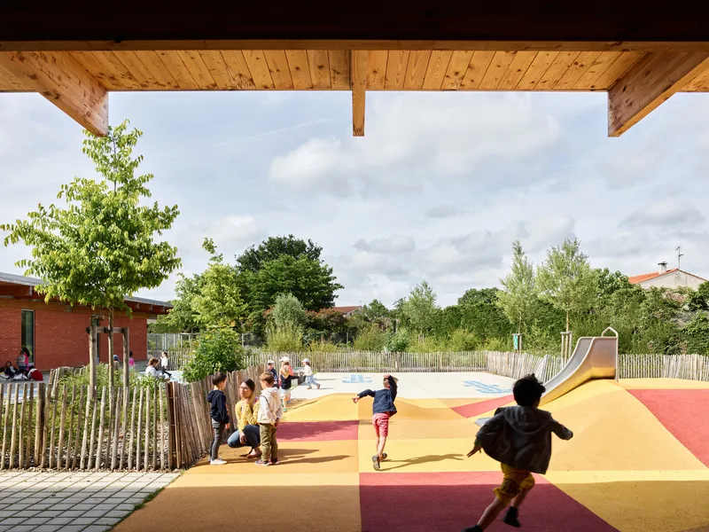 View from timber-clad porch toward playground with multicolored surfacing where children run and play