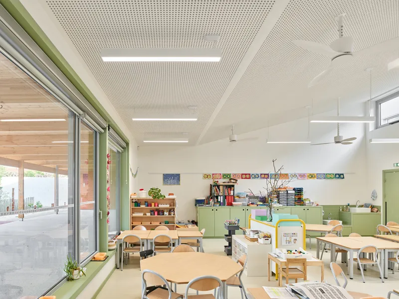Interior classroom with perforated acoustic ceiling, hexagonal tables, and green storage cabinets along the wall