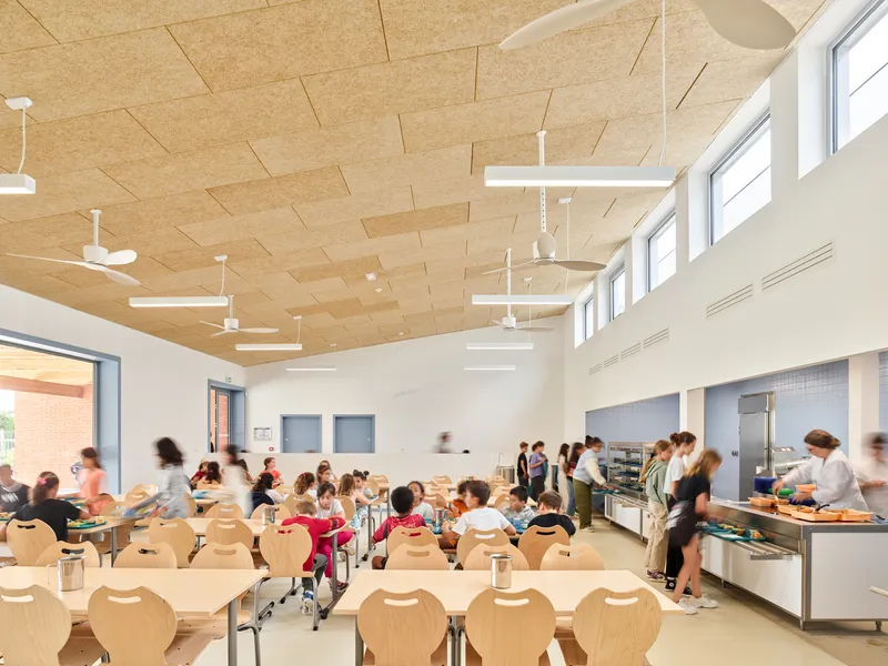 Dining hall with plywood ceiling panels and high clerestory windows filled with students at lunch