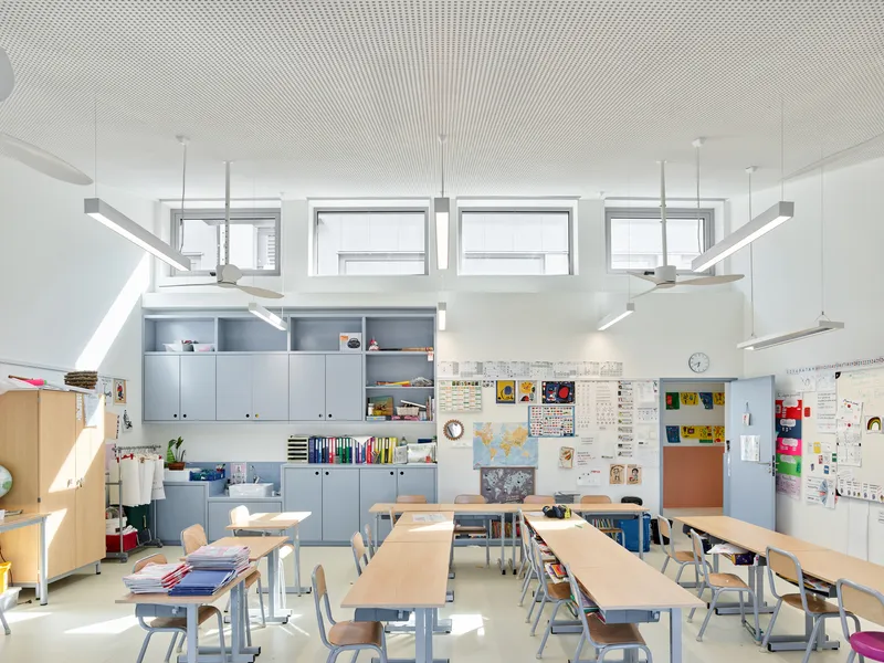 Classroom with perforated ceiling, grey storage units, and timber desks under clerestory glazing