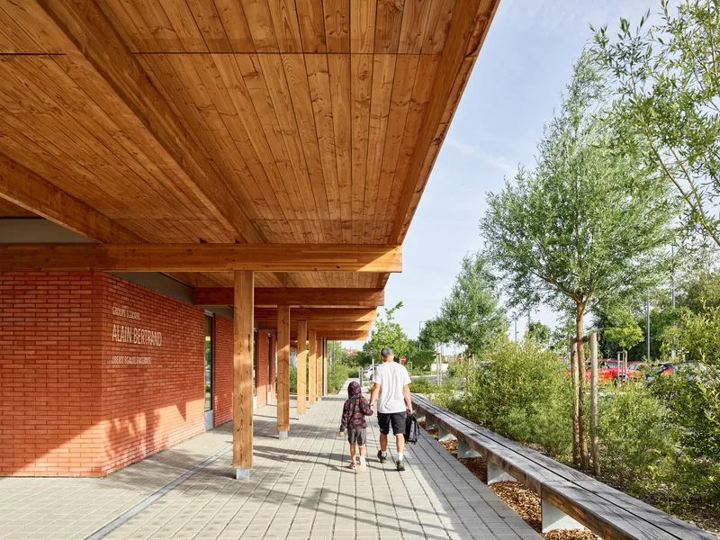 Timber-clad walkway with red brick wall and square columns casting shadows as a family walks past