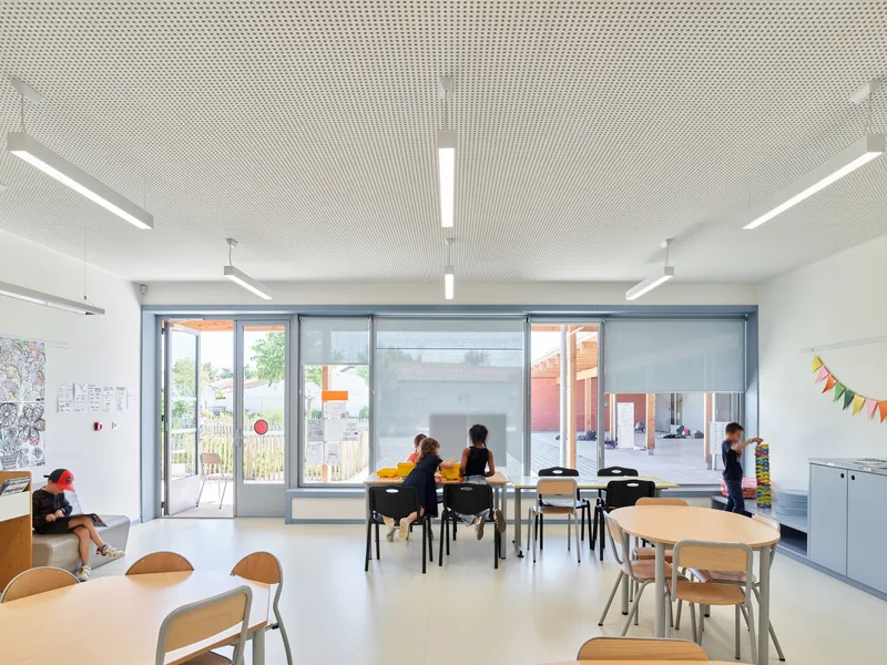 Classroom interior with perforated white ceiling panels and glazed doors opening onto a planted courtyard