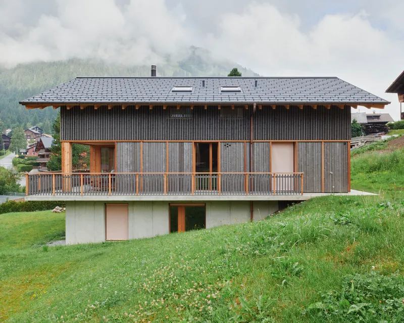 Slate-tiled roof and wooden balcony overlooking a grassy hillside with forested mountains in mist