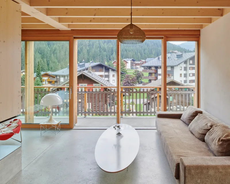 Living room with exposed timber ceiling beams and full-height glazing opening to a wooden balcony