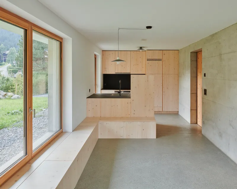 Kitchen with plywood cabinetry and black countertop alongside concrete walls and polished screed flooring
