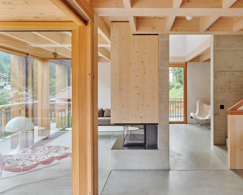 Central concrete fireplace core dividing open living spaces with timber beam ceiling and polished concrete floors