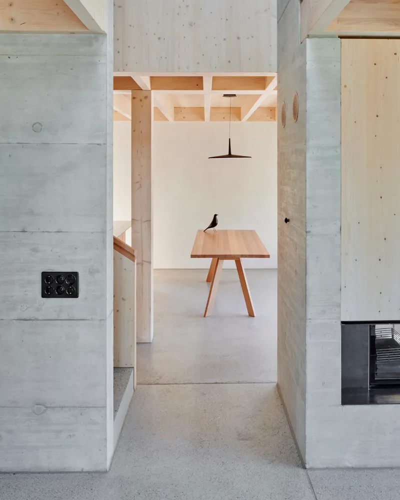 View through concrete walls into a dining area with exposed timber ceiling joists and pendant light