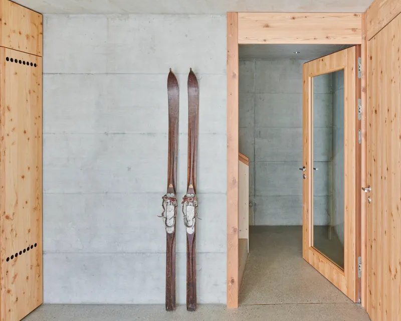 Pair of wooden skis leaning against a board-formed concrete wall beside timber-framed doorways