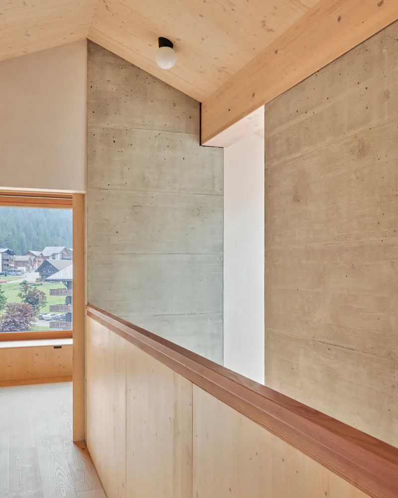 Timber handrail along concrete wall with window overlooking valley and village below