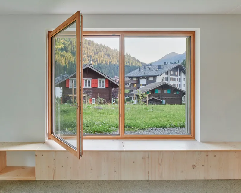 Interior view of timber-framed casement window opening to a meadow with village chalets and forested mountainside