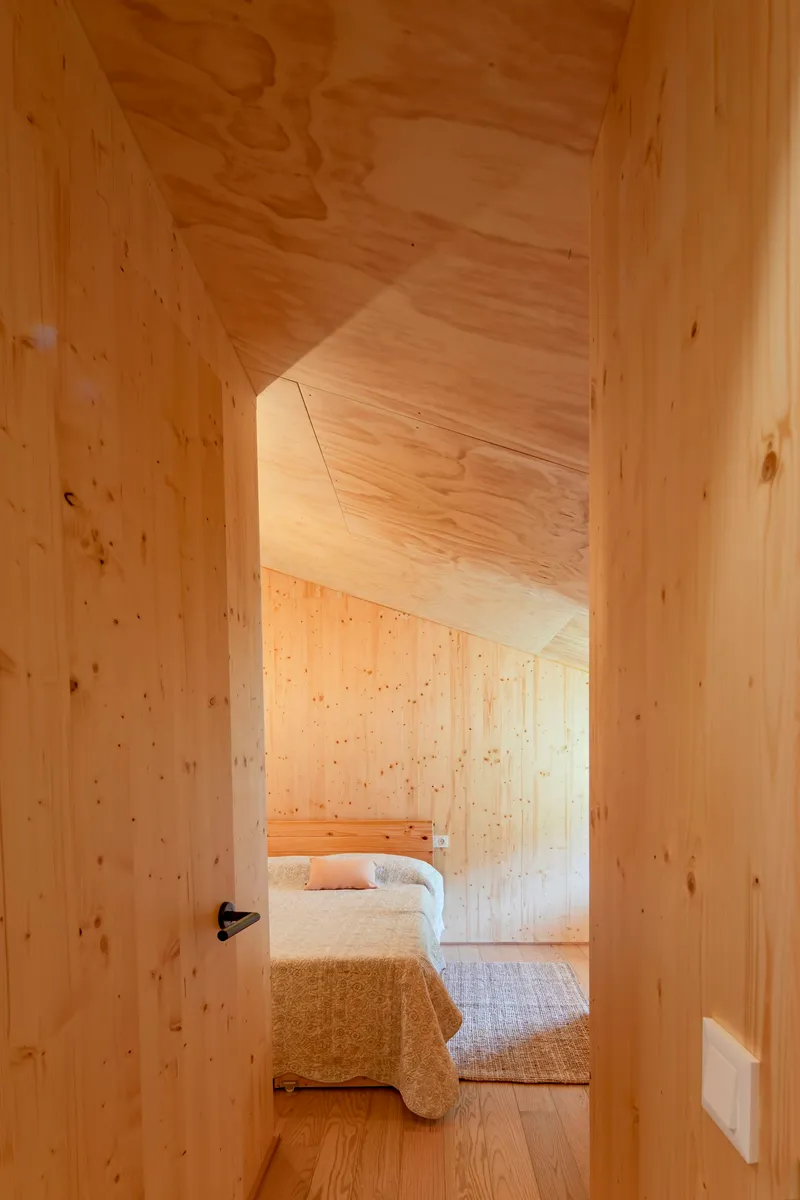 Timber-lined corridor leading through an angled doorway to a bedroom with natural daylight