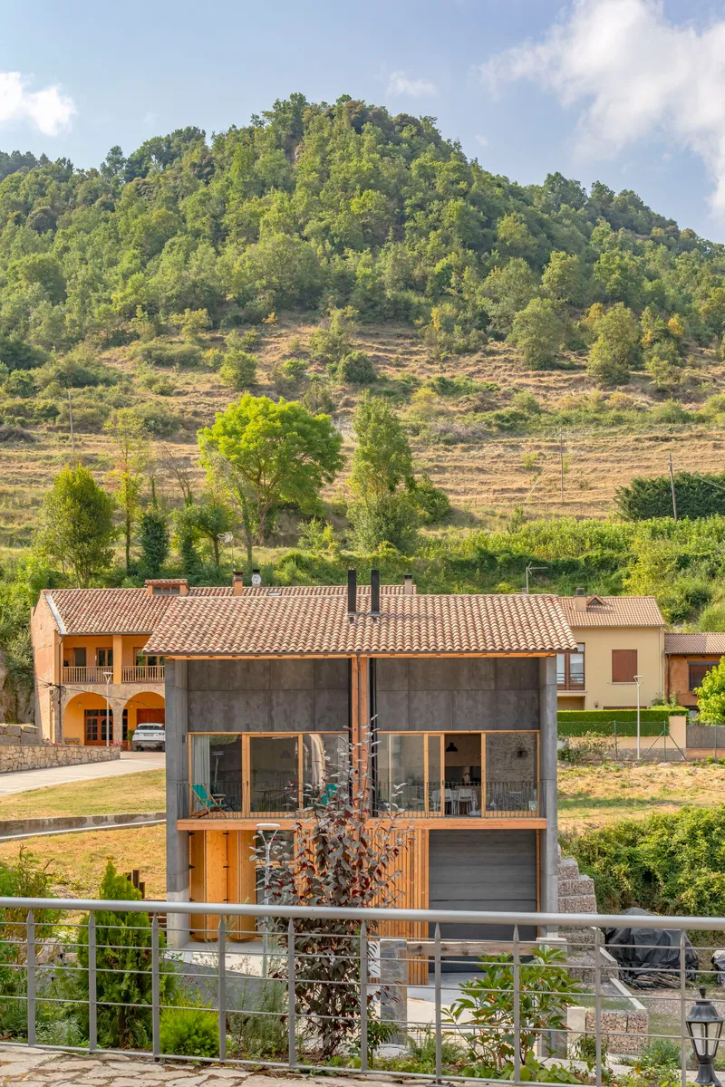 Concrete and timber house with exposed rafters beneath a terraced hillside planted with trees