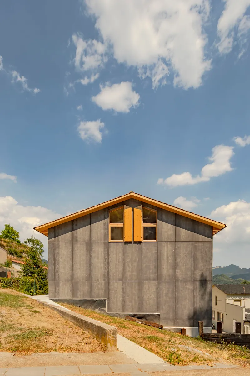 Gable end showing large-format concrete panels with timber trim window beneath a cloudy sky