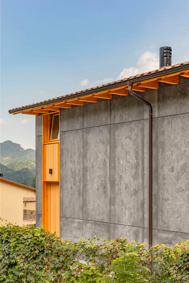Board-formed concrete wall with exposed timber roof rafters and a metal flue pipe