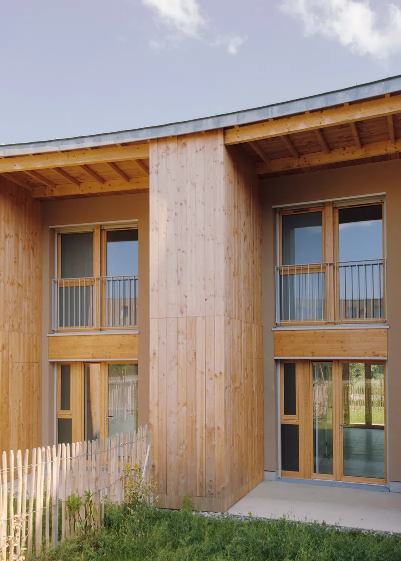 Timber-clad facade with exposed rafters and Juliet balconies at two levels beneath a cloudy sky