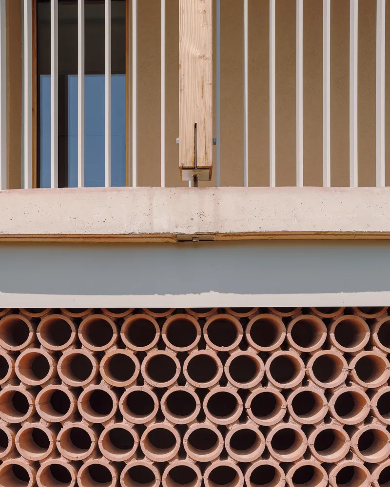 Facade detail showing terracotta tube screens below concrete beam and vertical timber slat cladding above