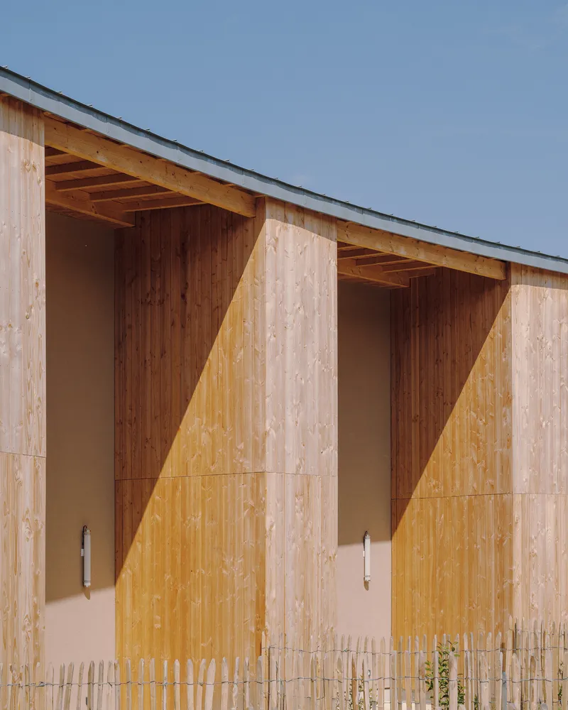 Close-up of timber facade panels with exposed rafters creating triangular shadow patterns in afternoon light