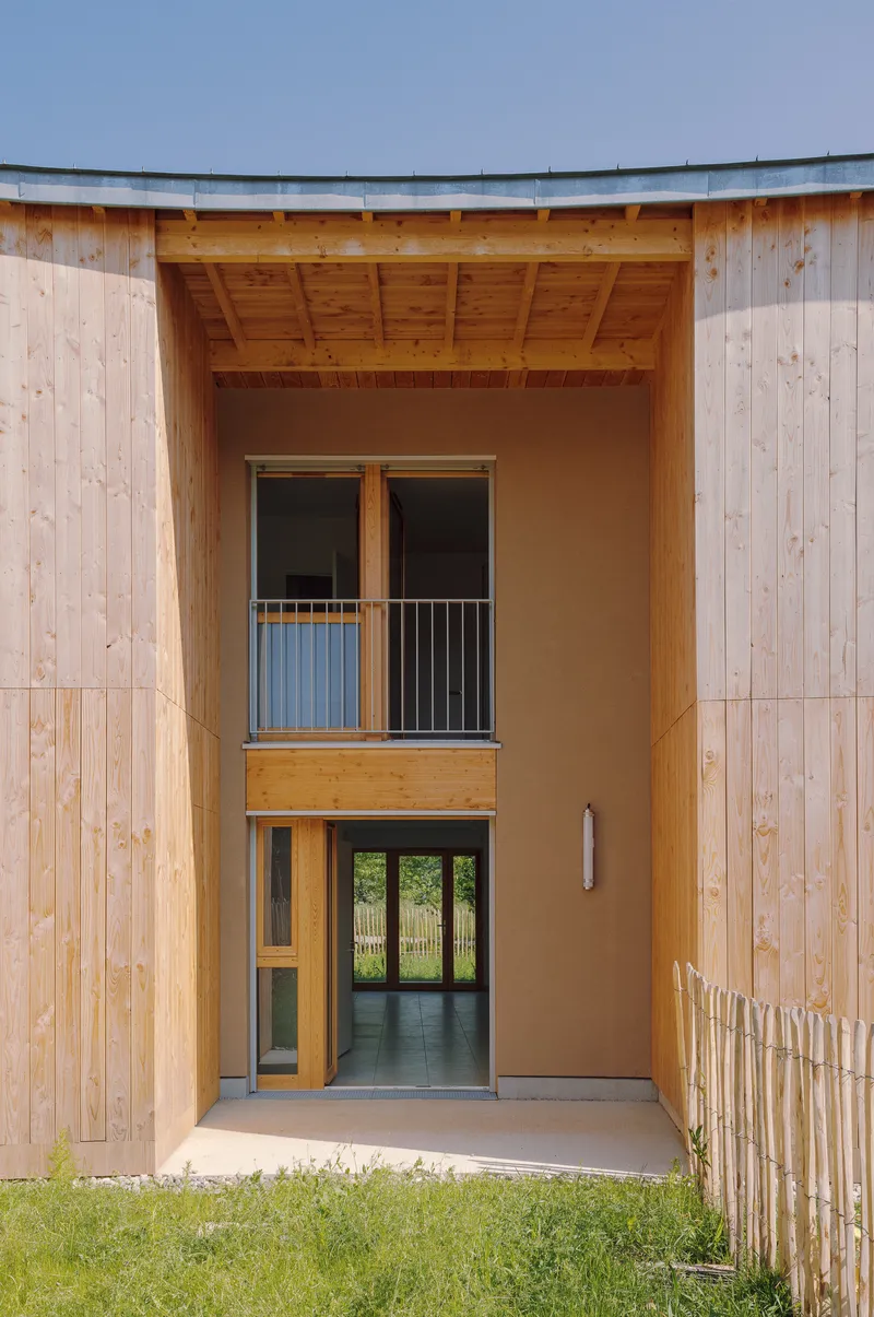 Double-height timber entrance recess with stacked glass doors and balcony framed by curved roof soffit