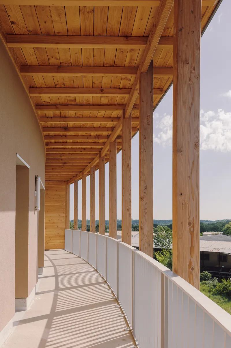 Covered timber walkway with exposed beams, white railing and vertical slats casting midday shadows