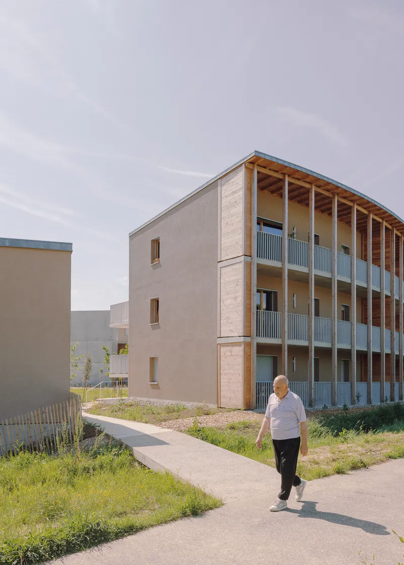 Three-storey timber and concrete block with open balconies and a resident walking along the pathway