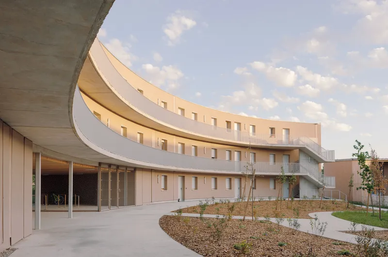 Courtyard view showing curving wings with pale stucco and timber facing a newly planted garden under clouds