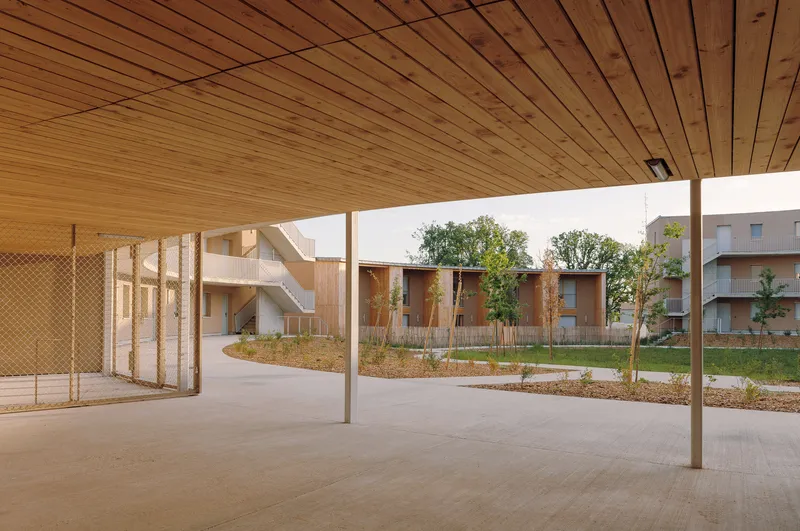 Covered porch looking across courtyard with timber columns, wood-slat ceiling and planted beds beyond
