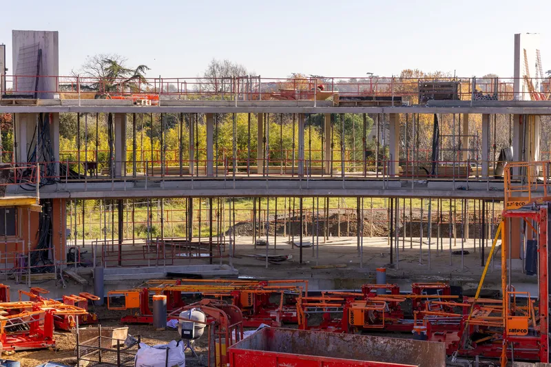 Construction view of the concrete floor slabs and steel columns with scaffolding and autumn trees beyond