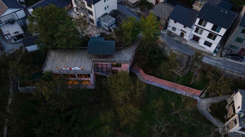 Aerial view of the timber deck roof and curved rammed earth wall amid dense tree cover