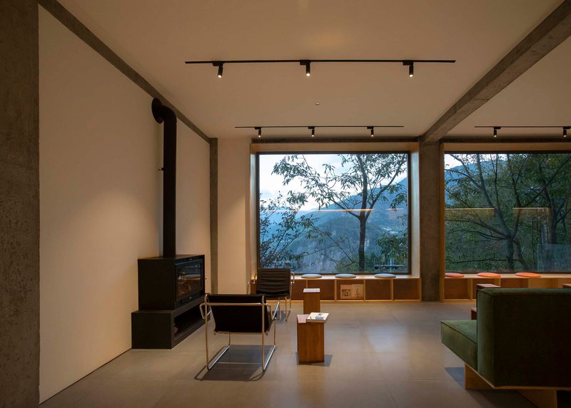 Interior lounge with exposed concrete beams, wood-framed window overlooking misty mountains, and black track lighting