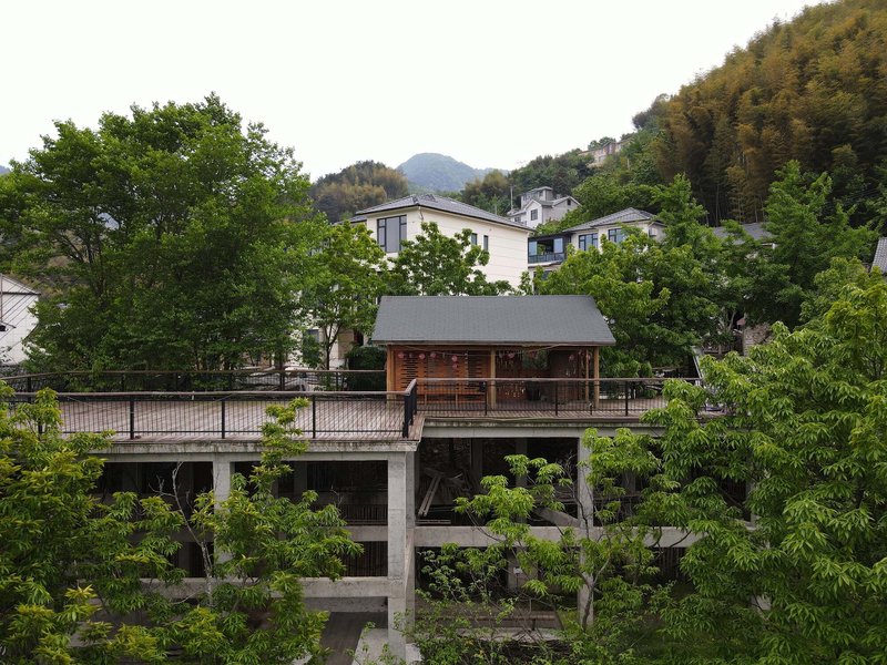 Timber pavilion with exposed wood columns and gridded facade on concrete base surrounded by green foliage