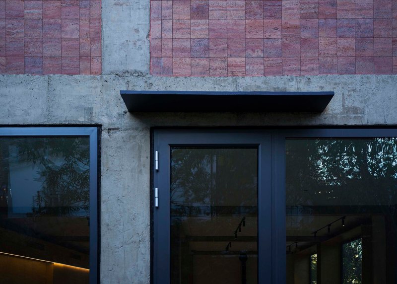 Black steel canopy over glass door set into concrete and rammed earth tile facade