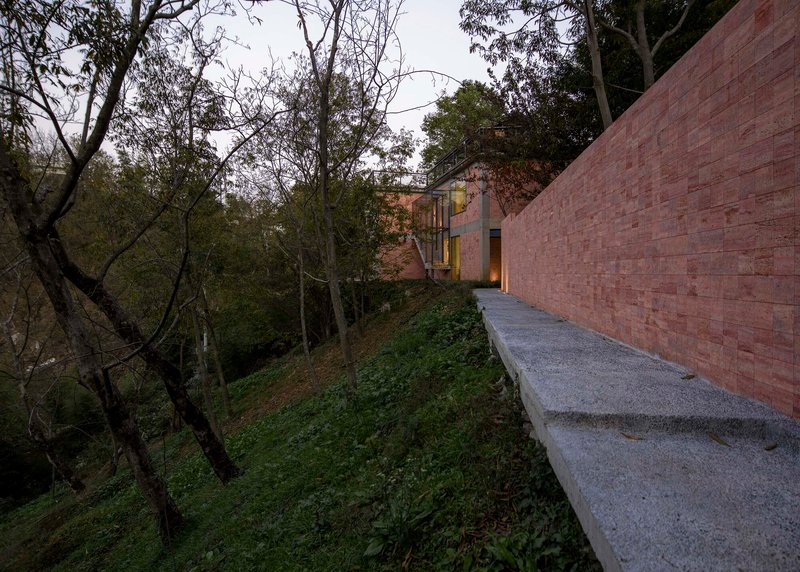 Elevated concrete walkway alongside a red stone facade with hillside trees in the background