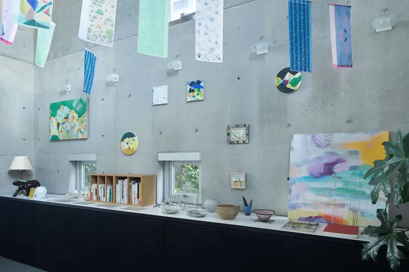 Board-formed concrete wall displaying paintings and artworks above black counter with potted plant