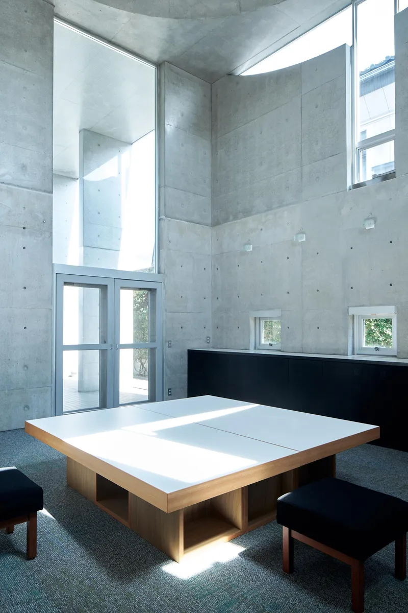 Low wooden table with white top surface beneath a tall concrete ceiling with clerestory glazing