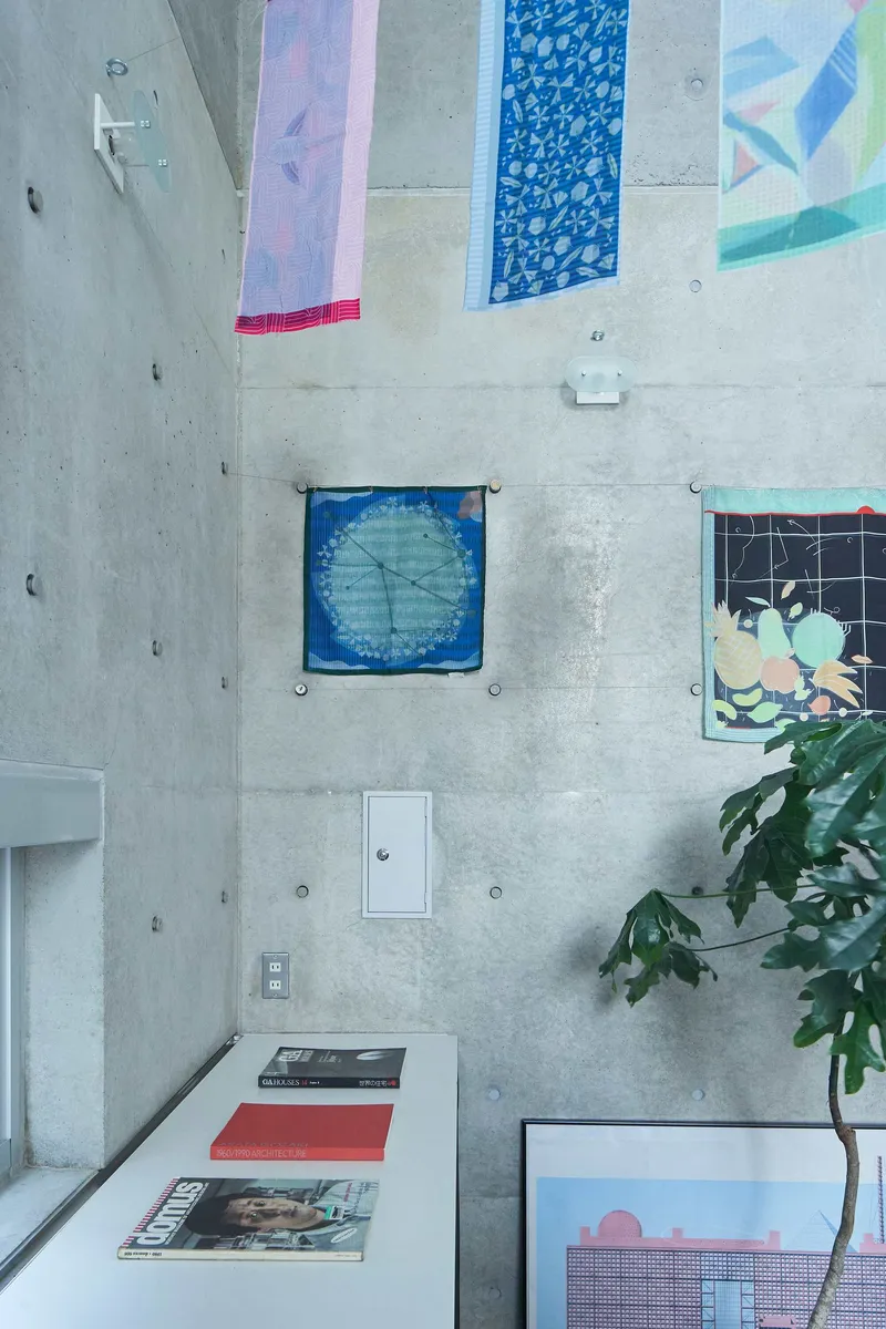 Overhead view of a white work surface with patterned fabric panels pinned to the concrete wall and a potted plant