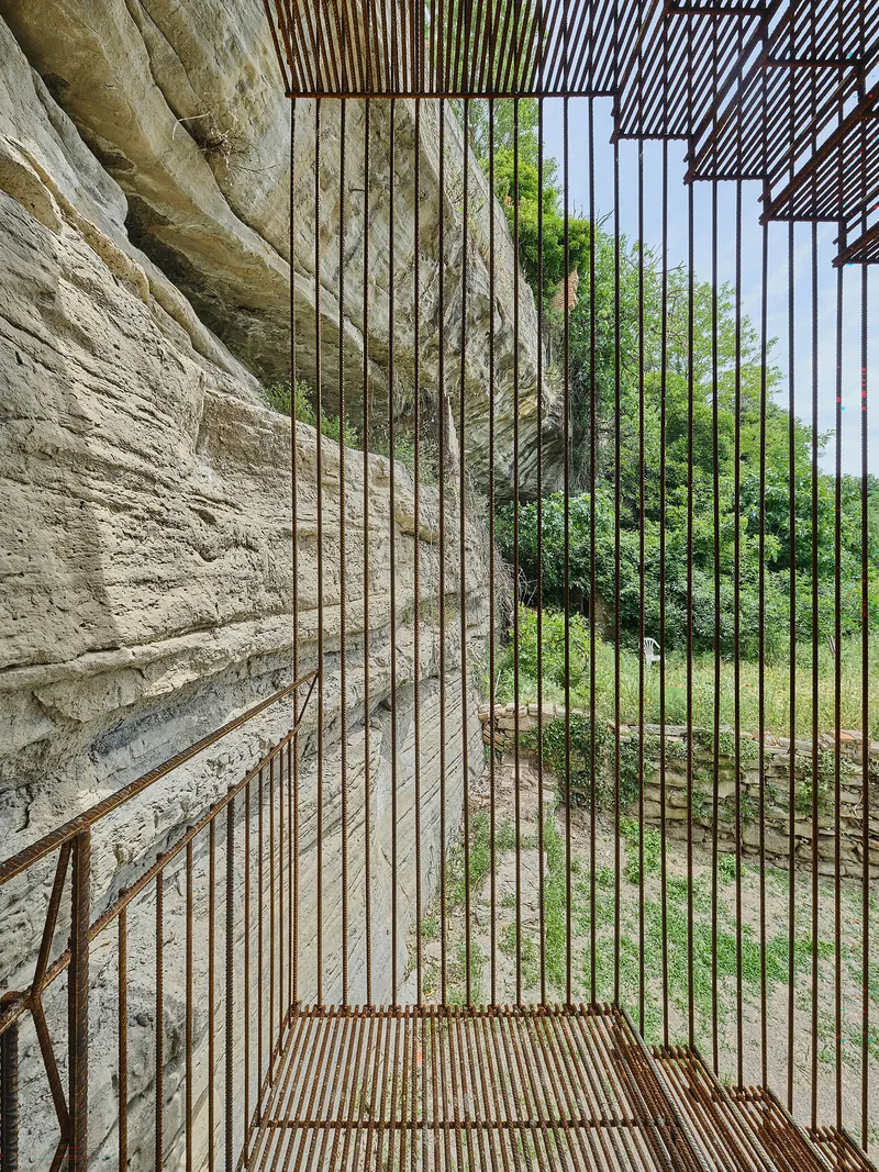 Interior view through vertical rod balusters with stone cliff face on one side and green landscape beyond