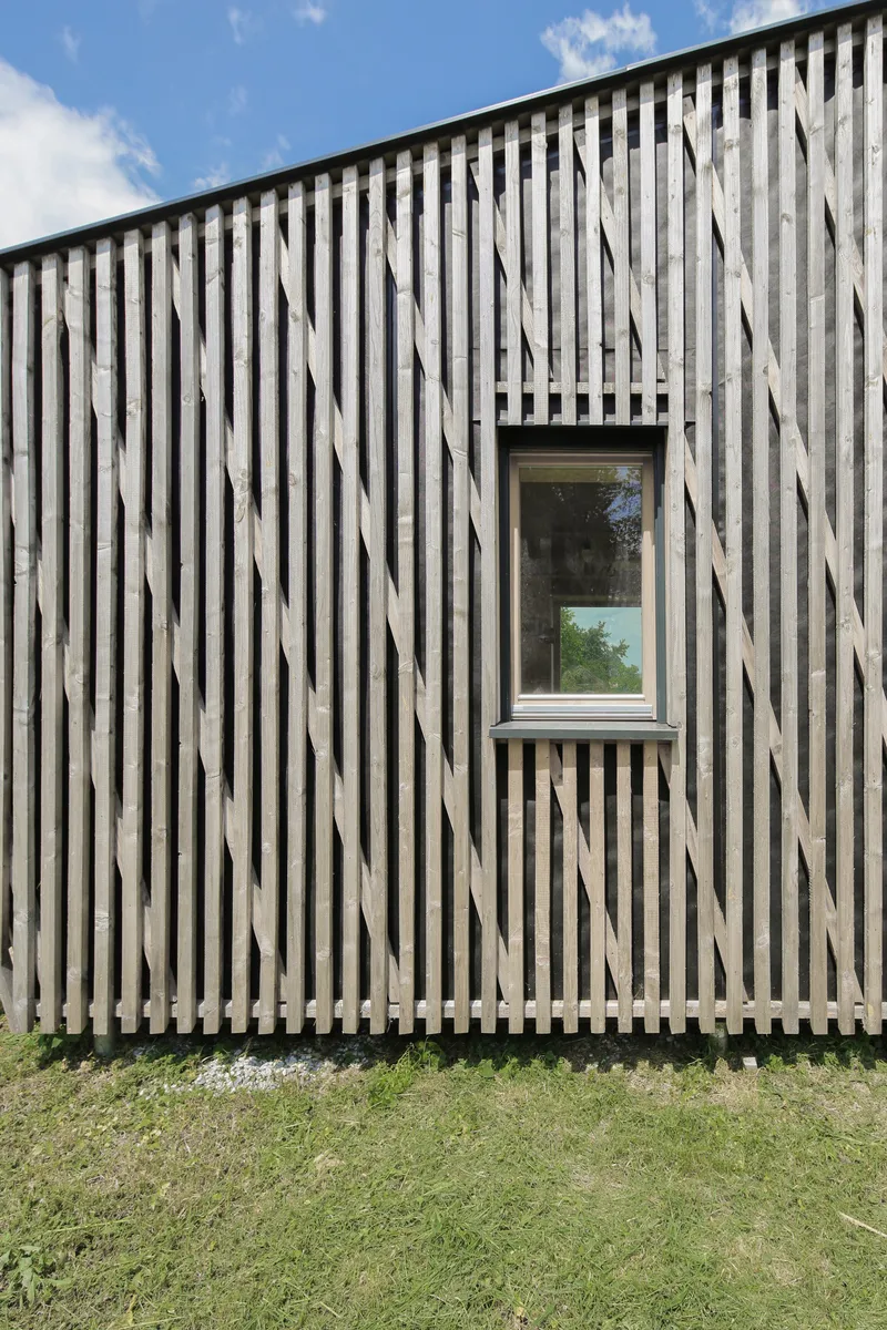 Weathered vertical timber slat facade with a single window under a clear sky