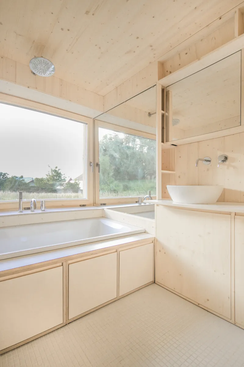 Pale plywood bathroom interior with built-in tub and basin beneath a sloped ceiling