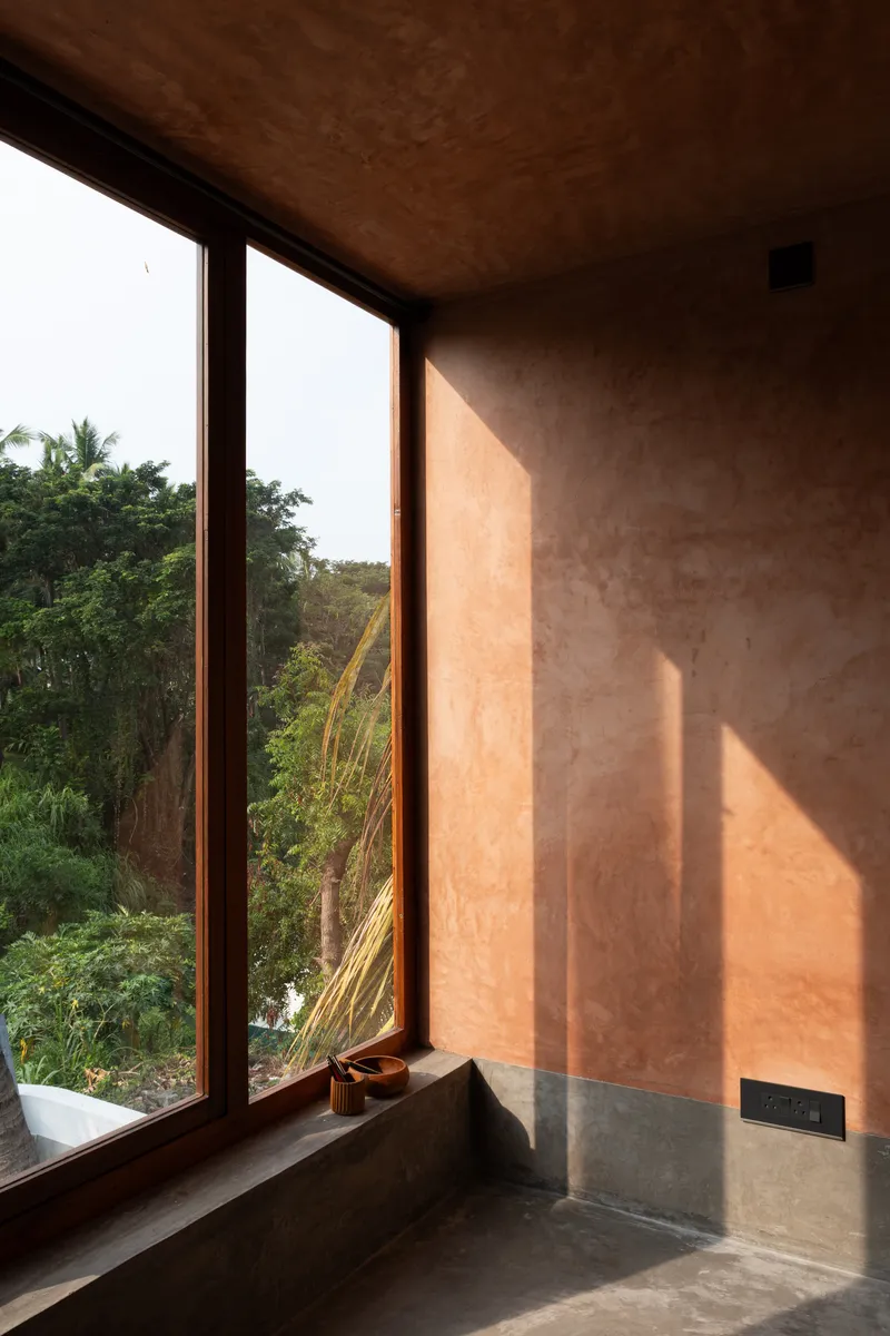 Corner window with timber frame casting afternoon light onto the pink plastered wall