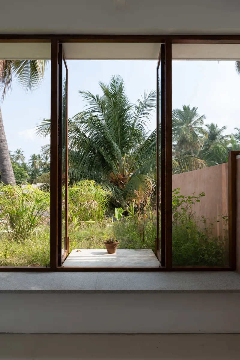 Interior view through timber-framed window opening to courtyard garden with palm trees beyond